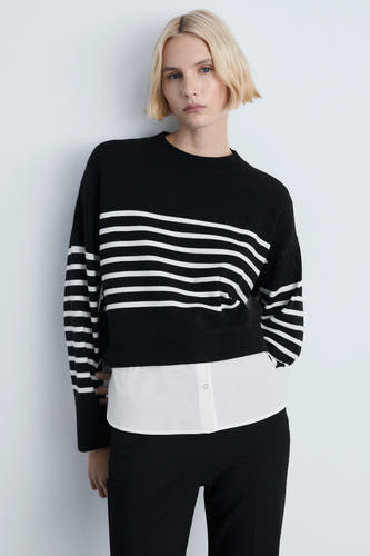 Zwarte trui met ronde hals van MANGO, met wit gestreept patroon en een witte blouse eronder, gecombineerd met een zwarte broek.
