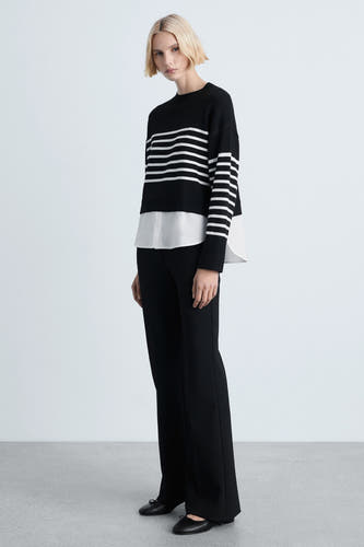 Zwarte trui met ronde hals van MANGO, gelaagd met een wit overhemd en gecombineerd met een zwarte pantalon en platte schoenen.
