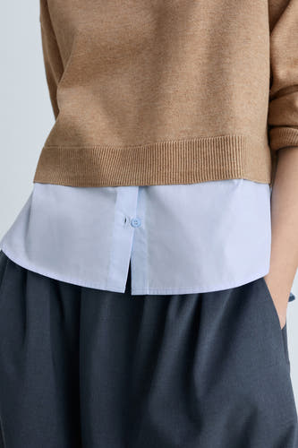 Bruine trui met ronde hals van MANGO, gestyled over een lichtblauw overhemd en een donkere broek.

