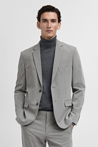 Grijze blazer van MANGO, gedragen over een donkergrijze coltrui en een broek in dezelfde kleur.
