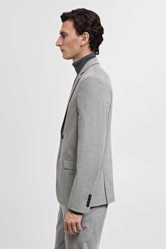 Grijze blazer van MANGO, zijaanzicht, gedragen over een grijze coltrui, met vier knopen op de mouw.
