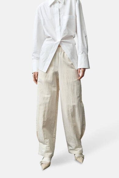 Ecru broek van MANGO, met wijde pijpen en elastische tailleband, gecombineerd met een wit overhemd en puntige pumps.
