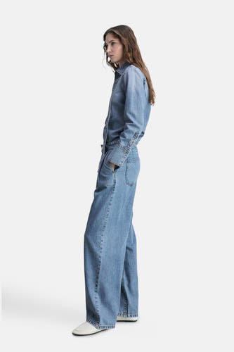 Jean en denim bleu mid, large de MANGO, avec des longues pattes et des chaussures blanches.
