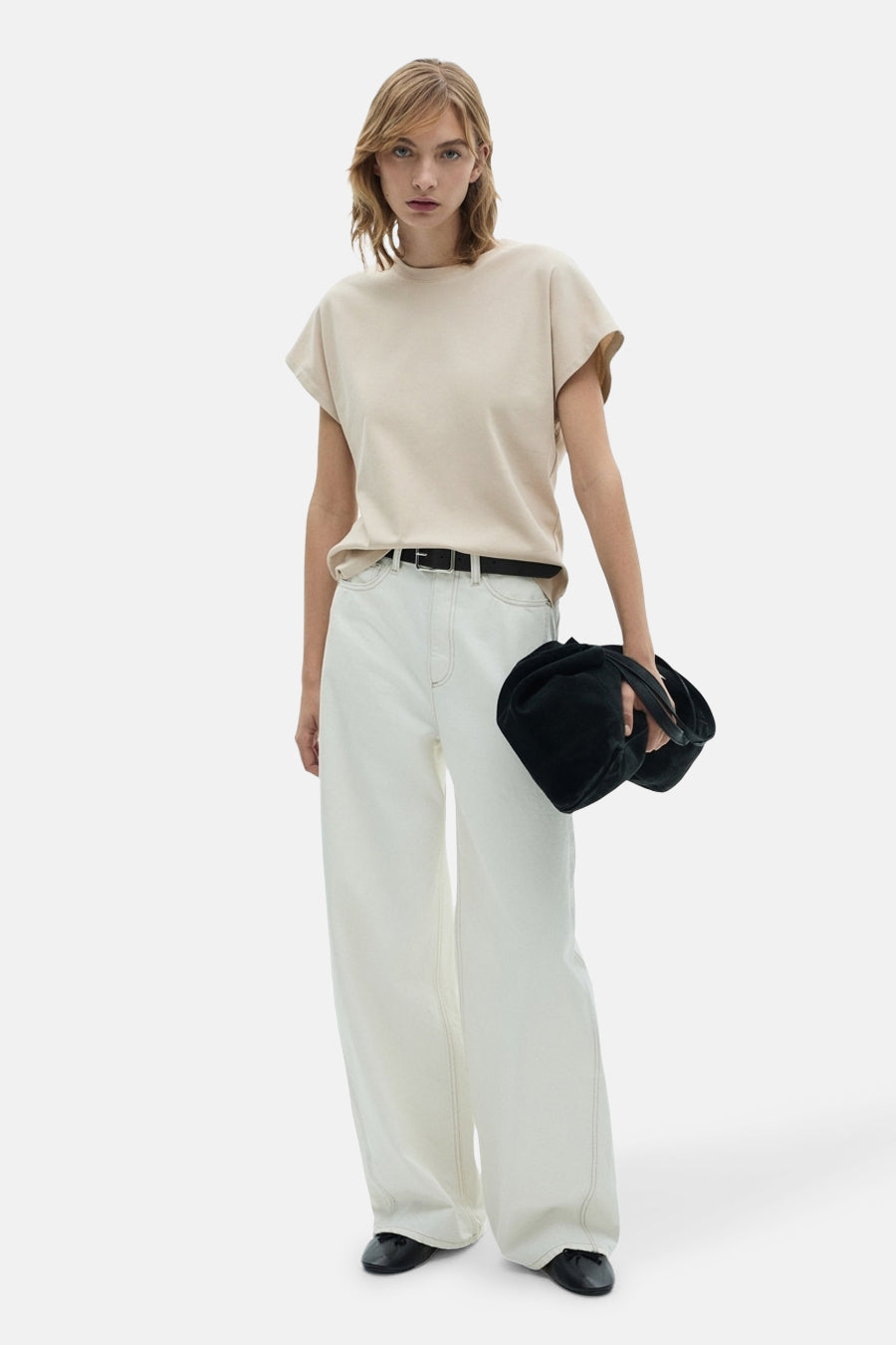 T-shirt beige à manches courtes de MANGO, porté avec un short blanc et une sacoche noire.