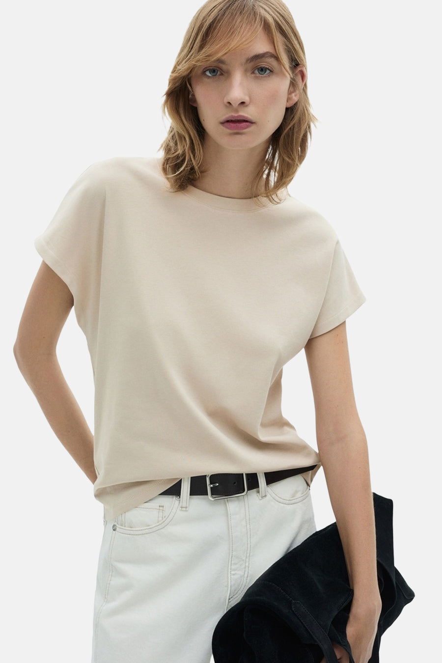 T-shirt beige à manches courtes de MANGO, porté avec des jeans blancs et une sac noir.