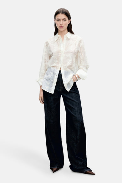 Vrouw in witte blouse en wijde jeans.