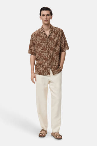 Chemise brune à manches courtes de MANGO, avec un motif, associée à une jupe crème et des sandales.