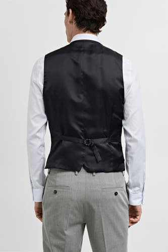 Gilet gris de MANGO, vu de de lrière avec une ce ajustableableableable le eté combin un un chemis blanc blanc et un pantalon gris.