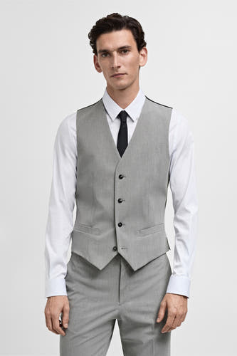 Gilet gris de MANGO porté sur une chemise blanche avec une cravate noire et un pantalon gris.