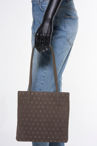 Bruine handtas van MANGO, met decoratieve zilverkleurige oogjes, gedragen over de schouder, gecombineerd met een blauwe jeans.