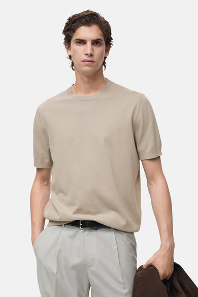 Beige T-shirt met korte mouwen van MANGO, gedragen met grijze pantalon en zwarte riem.