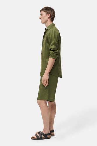 Groene short van MANGO, gedragen met een groen linnen overhemd en zwarte sandalen, in zij-aanzicht.
