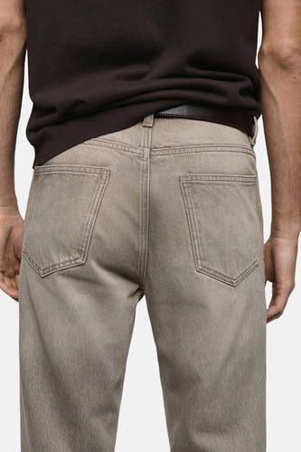 Grijze tapered jeans van MANGO, met achterzakken en een donkerbruine leren riem.
