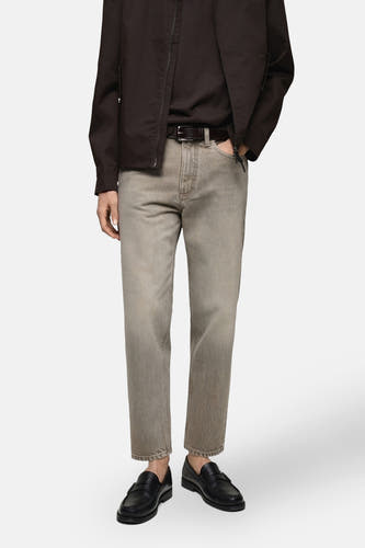 Tapered jeans van MANGO in middengrijs denim, gecombineerd met een bruine riem en zwarte leren loafers.