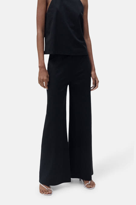 Zwarte broek van MANGO, met wijde pijpen en gecombineerd met een mouwloze top en witte sandalen.

