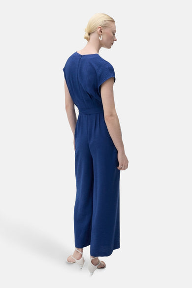 Combinaison bleue de MANGO, vue de derrière, avec des manches courtes et une ceinture à la taille.