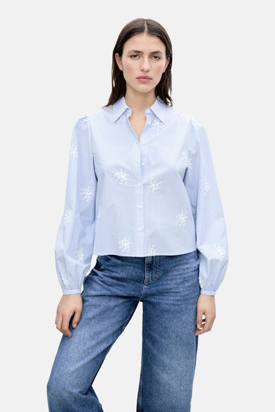 Blauw gestreept overhemd met lange mouwen van MANGO, afgewerkt met witte bloemenborduursels, gecombineerd met een jeans.

