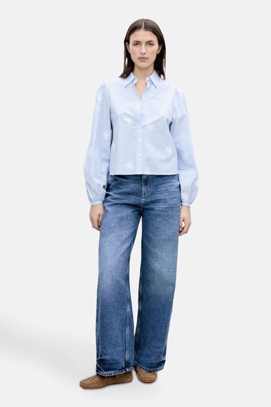 Blauw gestreept hemd met lange mouwen van MANGO, met witte bloemendetails en gecombineerd met wijde jeans en mocassins.
