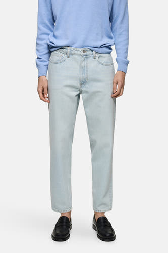 Lichtblauwe tapered jeans van MANGO, gecombineerd met een blauwe trui en zwarte loafers.