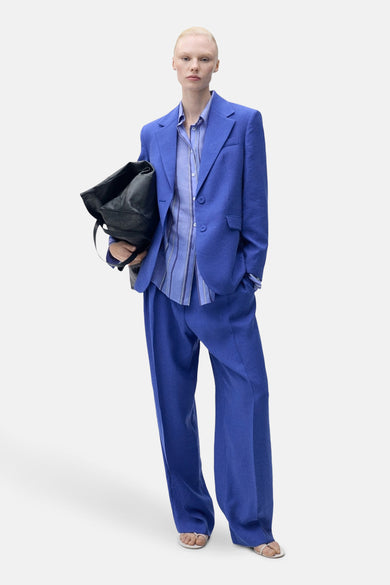 Blauwe kostuumbroek van MANGO, met wijde pijpen en gedragen met een blauw gestreept overhemd en zwarte tas.