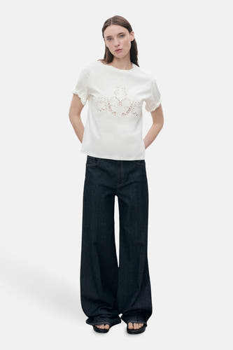 Witte T-shirt met korte mouwen van MANGO, met sierlijke broderie details op de borst en gedragen met wijde jeans.
