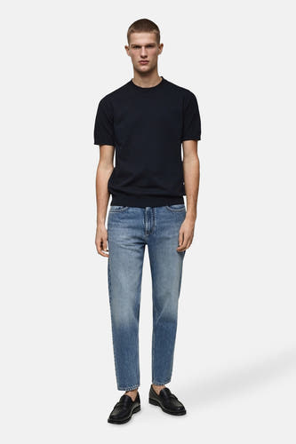Boutons de fermeture éclair sur des jeans en denim bleu MANGO, associés à un T-shirt bleu marine et à des loafers noirs.