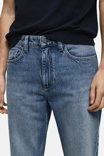 Boutons de fermeture à glissière sur des jeans MANGO en denim bleu moyen, avec poches et fermeture à glissière.