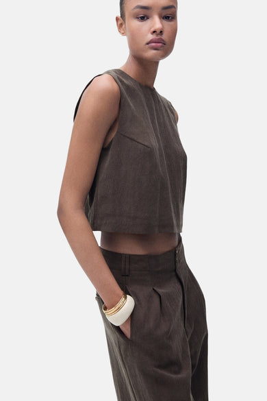 Bruine blouse zonder mouwen van MANGO, gecombineerd met een broek in dezelfde kleur en een witte armband.
