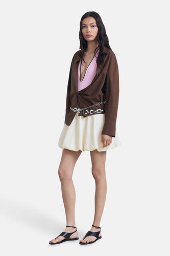 Ecru korte rok van MANGO, met een zilverkleurige kettingriem en gecombineerd met een bruin overhemd en zwarte sandalen.
