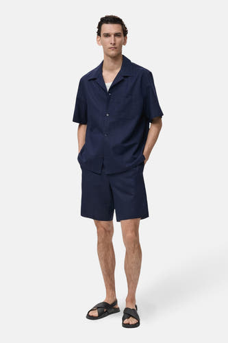 Chemise bleue à manches courtes de MANGO, portée avec un T-shirt blanc et une short coordonné.
