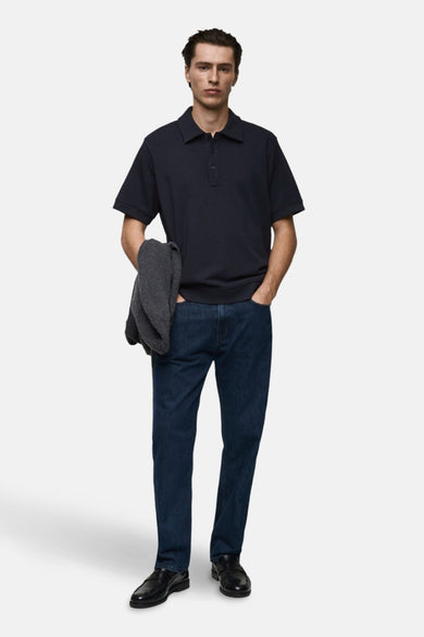 Man in donkerblauw poloshirt, jeans en zwarte schoenen.