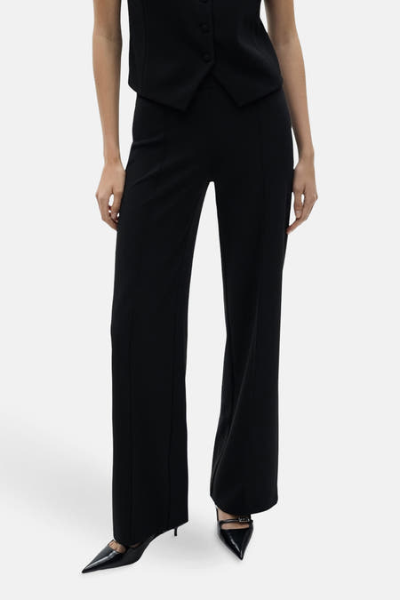 Zwarte broek van MANGO, met een uitlopend model en middennaad aan de voorkant, gecombineerd met zwarte pumps en een bijpassend vest.
