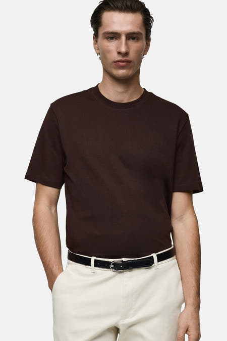Bruin T-shirt met korte mouwen van MANGO, gedragen met een witte pantalon en een zwarte riem.
