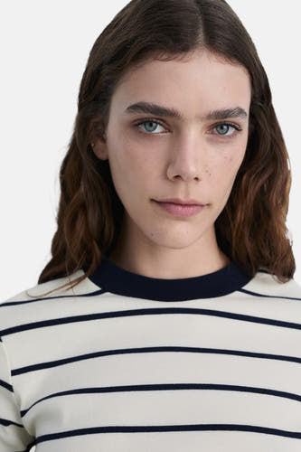 Wit gestreept T-shirt (korte mouwen) van MANGO, met een ronde halslijn en donkerbruin golvend haar.