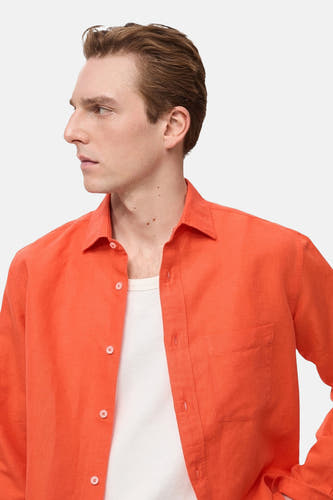 Chemise orange à manches longues de MANGO, avec une poche devant et un t-shirt blanc en dessous.