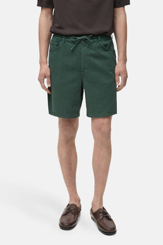 Short vert de MANGO, avec cordon et poches, associé à des chaussures brunes et un t-shirt brun.