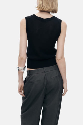 T-shirt sans manches noir de MANGO, vu de derrière, associé à un pantalon gris et un unmband argenté.