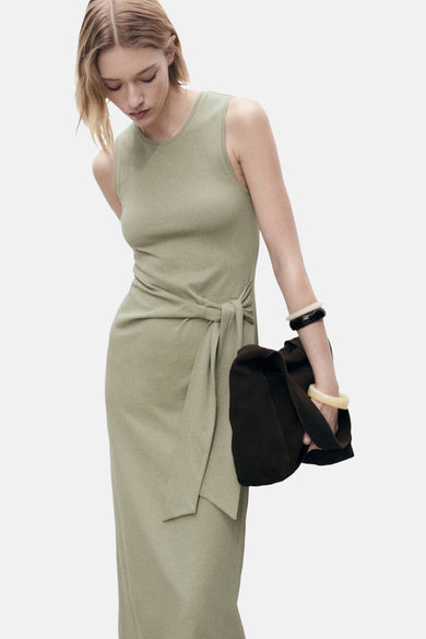 Khaki kleedje zonder mouwen van MANGO, met strikdetail en gecombineerd met armbanden en een donkerbruine tas.
