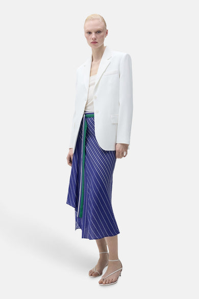 Longue jupe bleue de MANGO, avec des rayures blanches et une ligne d'arrêt asymétrique, associée à un gilet blanc.