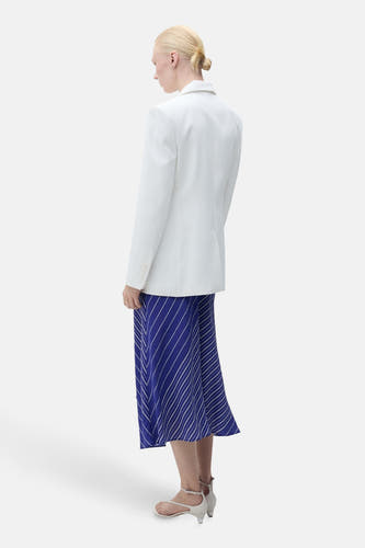 Lange blauwe rok met strepen van MANGO, gedragen met een witte blazer en sandalen met hak.