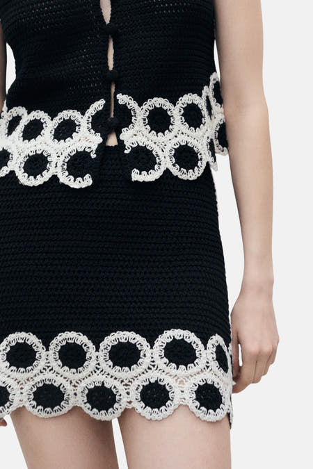 Jupe noire courte de MANGO, avec des détails effilochés en blanc cassé le long des bords.