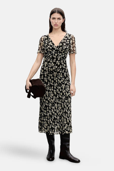 Robe noire à manches courtes de MANGO, avec un motif de marguerites et associée à des bottes noires.
