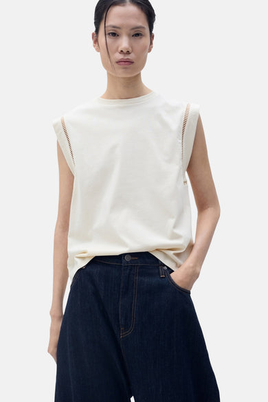 T-shirt sans manches beige de MANGO, avec des perforations décoratives sur les épaules et un jean bleu marine.