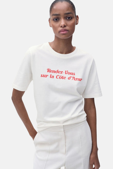 Wit T-shirt met korte mouwen van MANGO, met rode tekstprint op de borst, gecombineerd met een witte broek.
