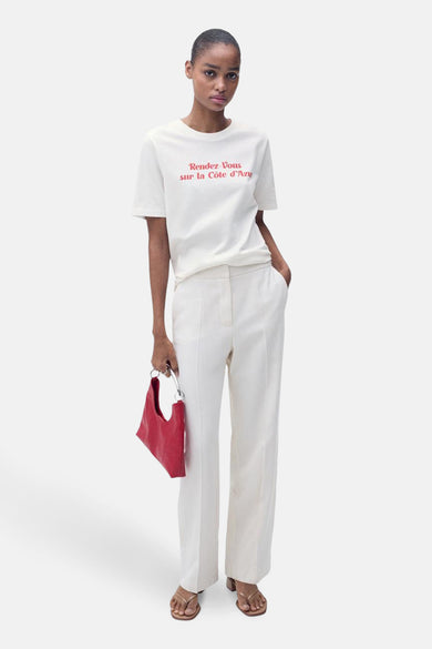 Wit T-shirt met korte mouwen van MANGO, met rode tekstprint en gecombineerd met witte pantalon en rode handtas.
