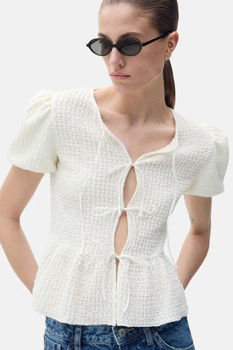 Witte blouse met korte mouwen van MANGO, met touwtjesdetails en gedragen met een blauwe jeans en zonnebril.
