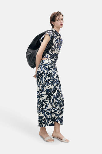 Multikleurige rok van MANGO met een bladerpatroon, gecombineerd met een bijpassende top en zwarte tas.
