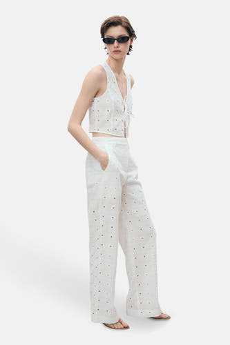 Witte blouse zonder mouwen van MANGO, met broderie details, gedragen met een bijpassende broek en zonnebril.
