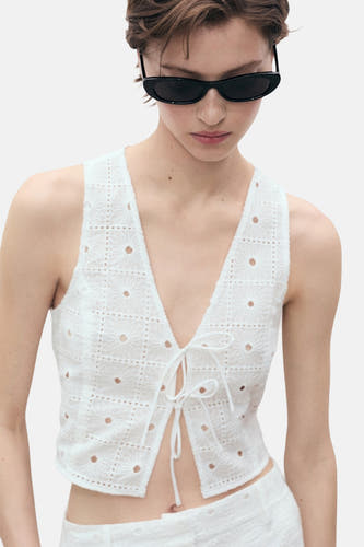Witte mouwloze blouse van MANGO, met openwork details en een striksluiting aan de voorkant.
