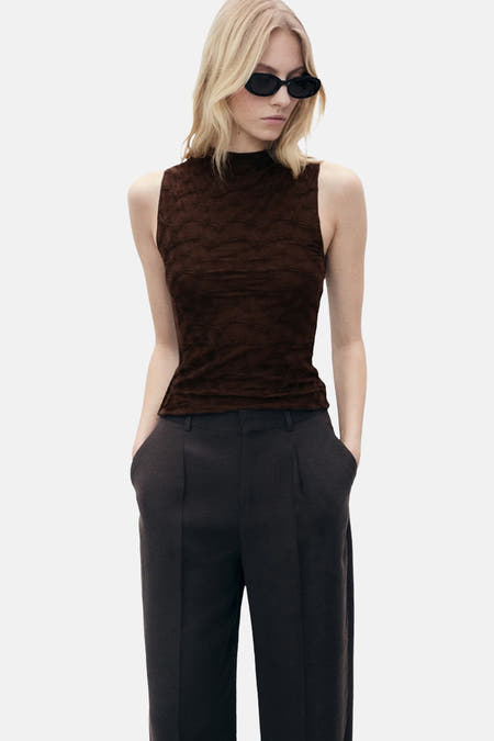Bruine mouwloze blouse van MANGO, met een subtiel patroon en gecombineerd met een donkere pantalon.